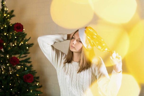 Ευτυχισμένος έφηβος κορίτσι σε ένα χρυσό καπέλο Χριστούγεννα χαζολογώντας γύρω από ένα χριστουγεννιάτικο δέντρο - Φωτογραφία, εικόνα