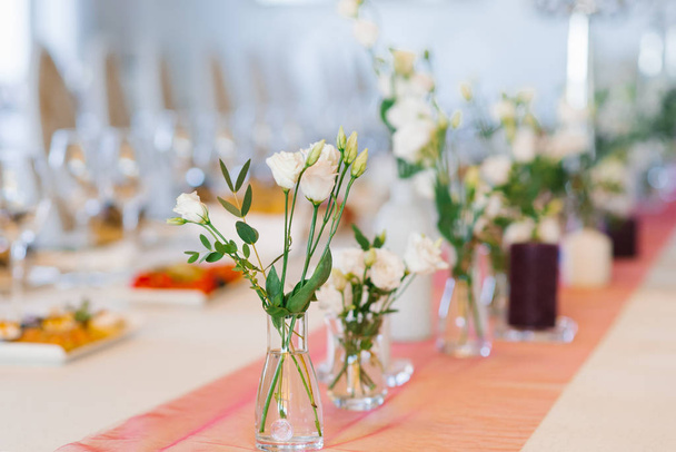 Białe kwiaty eustoma stoją w szklanych wazonach na świątecznym stole na weselu - Zdjęcie, obraz