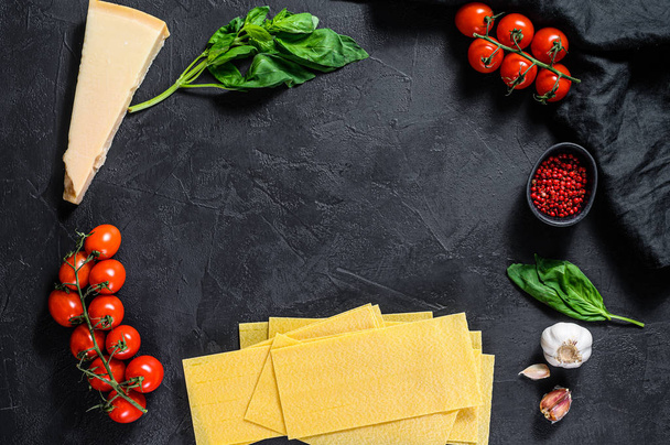 Het concept van lasagne koken. Ingrediënten, lasagne lakens, Basilicum, kerstomaten, Parmezaanse kaas, knoflook, peper. Zwarte achtergrond. Bovenaanzicht. Ruimte voor tekst - Foto, afbeelding