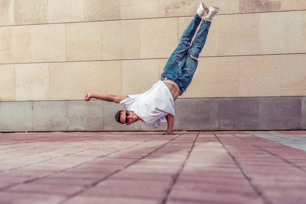 male athlete, motion flies on one arm, summer city, hip-hop style, break dancer. Free space motivation text. Active youth lifestyle, modern fashionable hipster street dancer. T-shirt jeans sunglasses. - Foto, imagen