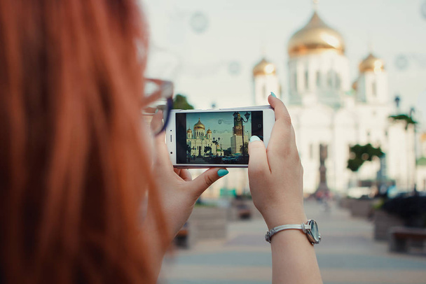 Telefondaki kızıl saçlı kız fotoğrafları Rostov-on-Don 'daki Ortodoks kilisesi. - Fotoğraf, Görsel