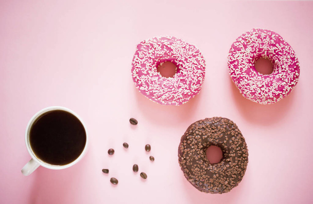 ピンクのアイシングと粉末のおいしいドーナツ白い木製の背景に芳香族コーヒーのカップ. - 写真・画像