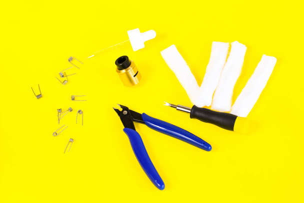 elektronische sigarettendetails, Vata, spoelen, druppelinfuus, veer, nippers op een gele achtergrond. vlakke leghendel - Foto, afbeelding