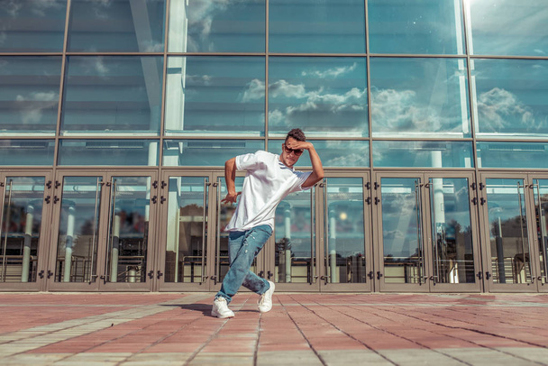 Male athlete dancing glass window background, summer city, hip hop style, break dancer. Free space motivation text. Active youth lifestyle, modern fashionable street dancer. T-shirt jeans. - Photo, Image