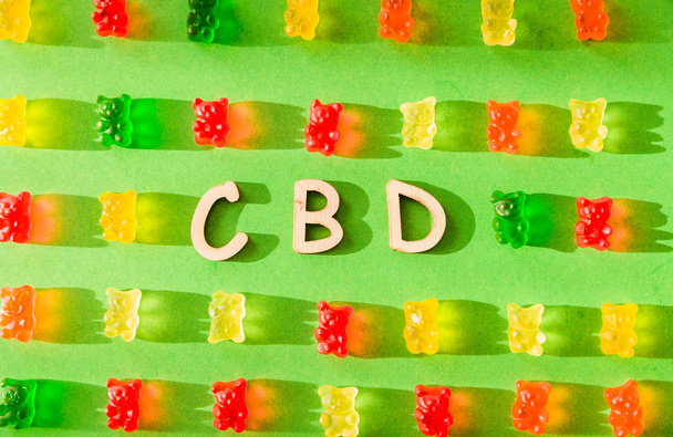 Lettere in legno CBD su sfondo verde e gelatina sotto forma di orsi. Vista dall'alto. L'ombra del sole cade sullo sfondo
 - Foto, immagini