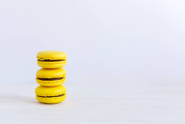 Três macarons franceses amarelos em uma mesa de madeira. Macarons de banana com creme de chocolate
.  - Foto, Imagem