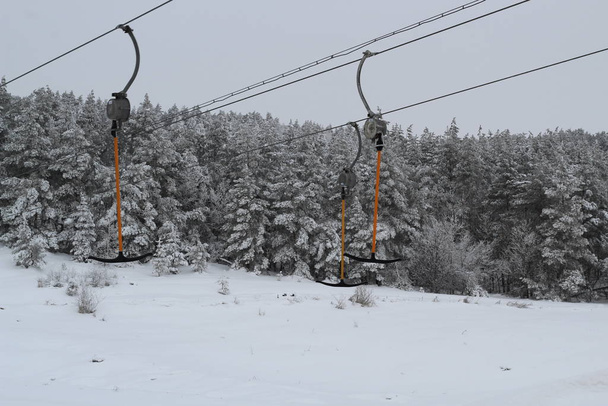 Skilift voor skiërs en snowboarders met stokken in de winter op een besneeuwde heuvel - Foto, afbeelding