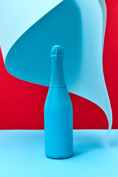 Holiday composition of painted blue wine mock up bottle on a duotone background with folded sheet of blue paper, copy space. - Фото, зображення