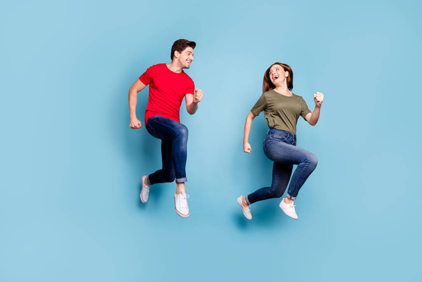 Full length photo of charming spouses relax rest jump run wear green red t-shirt denim jeans sneakers isolated over blue color background - Foto, Imagem