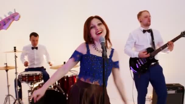 A musical band of four people playing song in the bright studio - filming a music video - men wearing white shirts and a woman wearing colorful dress - Materiał filmowy, wideo