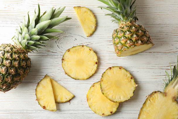 Ananas a plátky na bílém dřevěném pozadí, pohled shora - Fotografie, Obrázek