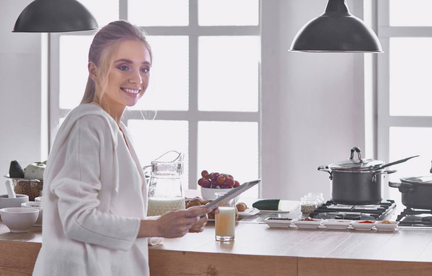 gyönyörű fiatal nő használ egy digitális tabletta a konyhában - Fotó, kép