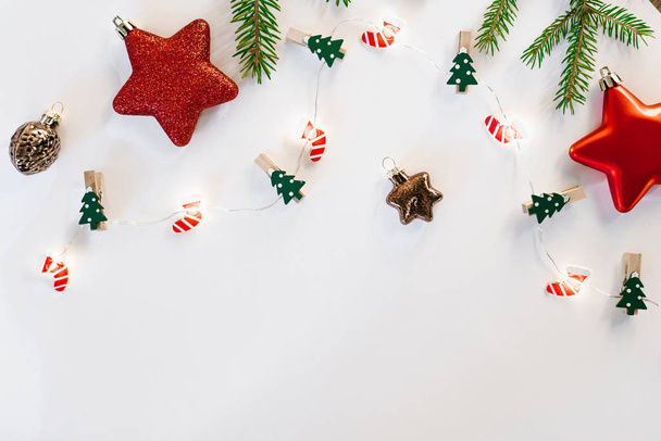 現代のクリスマス作品。クリスマスのおもちゃ、茶色と赤の装飾、トウヒの枝、白い背景のお祝いのライト。フラットレイアウト、トップビュー。コピースペース付きの休日カード - 写真・画像