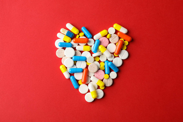 Heart made of pills on red background, space for text. Top view - 写真・画像