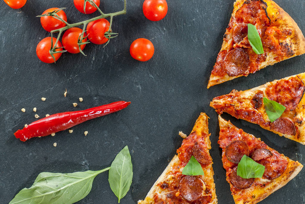 deliziose fette cotte fresche di pizza piccante su ardesia con pomodorini peperoncino e foglie di basilico
 - Foto, immagini
