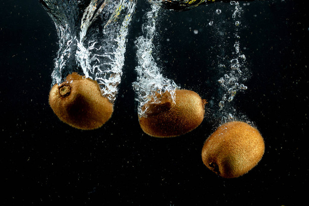 three kiwis splashing into water in black background - Foto, Bild