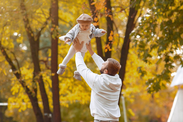 Knappe vader in een grijze trui spelen met kleine dochter in een herfst park - Foto, afbeelding