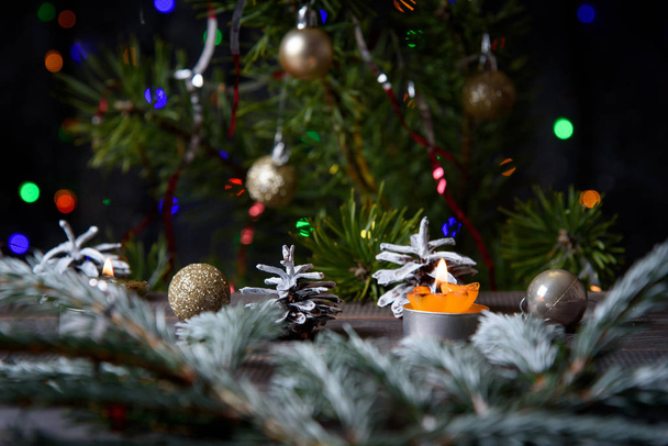  Kerst, decoratie op een houten tafel. Kerstdennenappels en gouden kerstballen. Brandende kaars - Foto, afbeelding