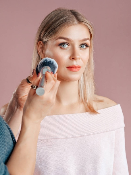 Verticaal portret shot make-up kunstenaar brengt gezichtspoeder op een vrouwelijk gezicht op een heldere achtergrond. Bruiloft make-up concept - Foto, afbeelding