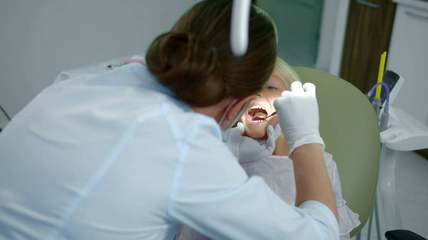 Дантист смотрит на женские зубы с маленьким зеркалом
. - Фото, изображение