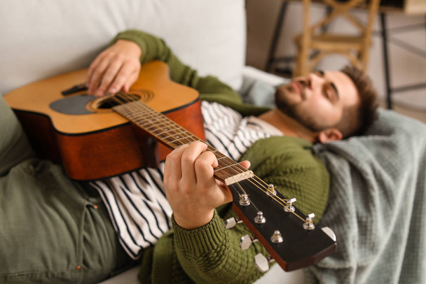 Handsome young man playing guitar at home - Foto, afbeelding