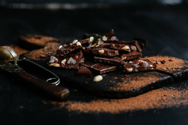 Шматочки молочного шоколаду з горіхами та сухофруктами на дерев'яній дошці
 - Фото, зображення