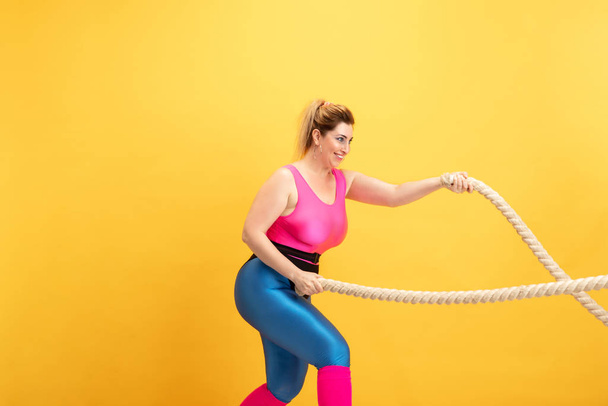 Young caucasian plus size female models training on yellow background - Foto, Imagen