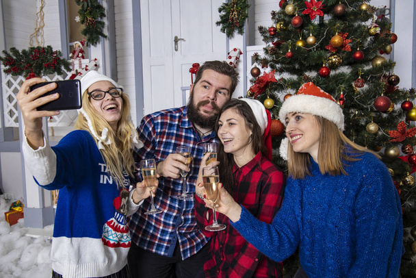 Рождественская компания веселое настроение улыбаясь фотогеничные люди делают селфи в зимние праздники праздничные украшенные фона интерьера
 - Фото, изображение