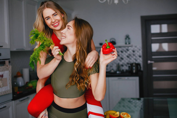 Two sports girl in a kitchen with vegetables - Foto, Imagen
