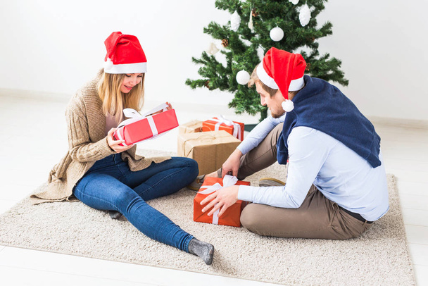 Noël et vacances concept - Jeune couple heureux portant chapeaux santa cadeaux d'ouverture à la maison
. - Photo, image
