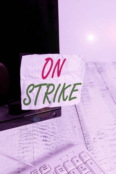 Handwriting text On Strike. Concept meaning refuse to continue working because of an argument with an employer Notation paper taped to black computer monitor screen near white keyboard. - Photo, Image