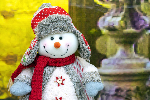 セーター、赤いスカーフ、帽子の中の雪だるまのクリスマスの柔らかいおもちゃ. - 写真・画像