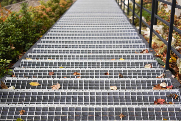 neue Treppe aus Metall oder Stahl mit Löchern in den Stufen und abgefallenen gelben Blättern. schwarzes Geländer entlang der Treppe. Herbstlandschaft - Foto, Bild