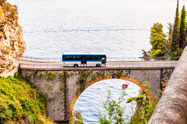 View on Fiordo di Furore arc bridge built between high rocky cliffs above the Tyrrhenian sea bay in Campania region. Bus driving on the bridge, boat floating by the unique cove under - Photo, Image