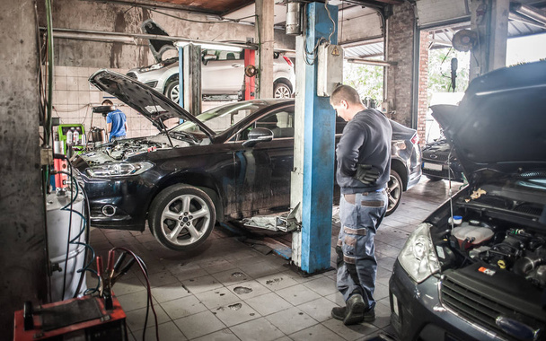Mecánico de coches trabajando en un garaje de reparación con elevador de coche hidráulico
 - Foto, imagen