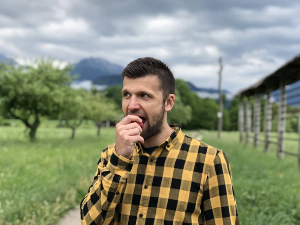 jóképű férfi alkalmi ruhákban szórakozik és barackot eszik, miközben a hegyek között sétál a nyári napon   - Fotó, kép