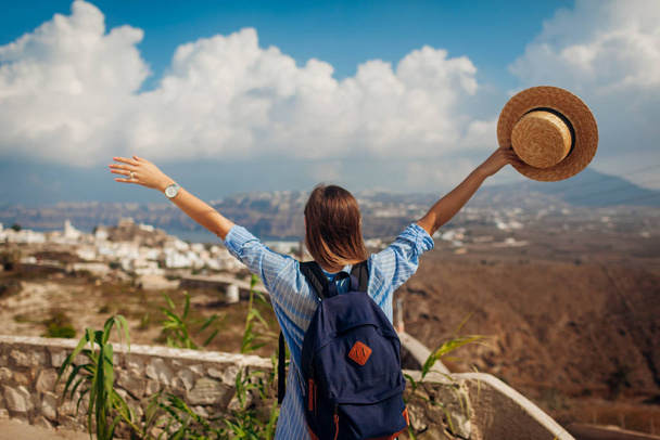 Santorini traveler with backpack raised arms feeling happy looking at Akrotiri, mountains landscape on island. Tourism - Foto, Imagen