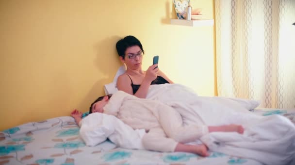 A young mother lies on the couch and uses a smartphone. - Πλάνα, βίντεο