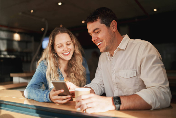 Lovely smiling young couple on date enjoying browsing the mobile apps at coffee shop counter - Foto, Bild