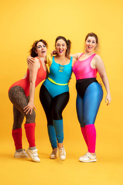 Young caucasian plus size female models training on yellow background - Foto, imagen