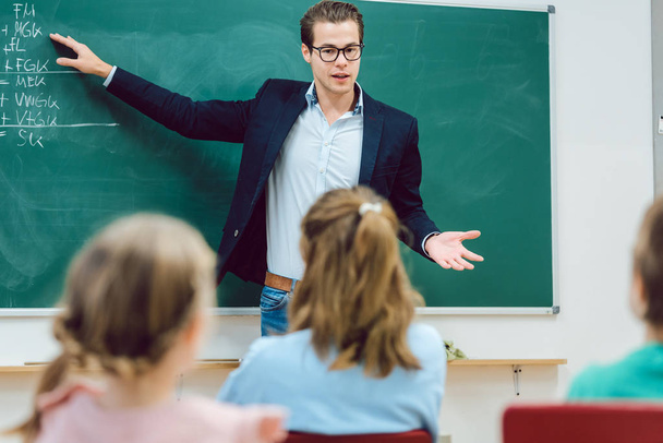 Teacher standing in front of students in school class - Foto, afbeelding