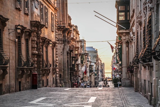Valletta, maltański krajobraz miejski. Wąska ulica w Valletta - stolicy Malty. Tradycyjna maltańska architektura. Stara historyczna część La Valetta z ludźmi na zewnątrz i wąskimi uliczkami, Malta - Zdjęcie, obraz