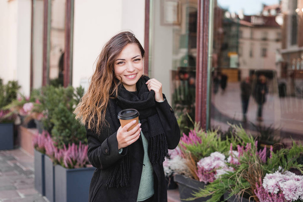 Mano femenina con taza de papel de café para llevar. Mujer sosteniendo taza en el fondo urbano
 - Foto, Imagen
