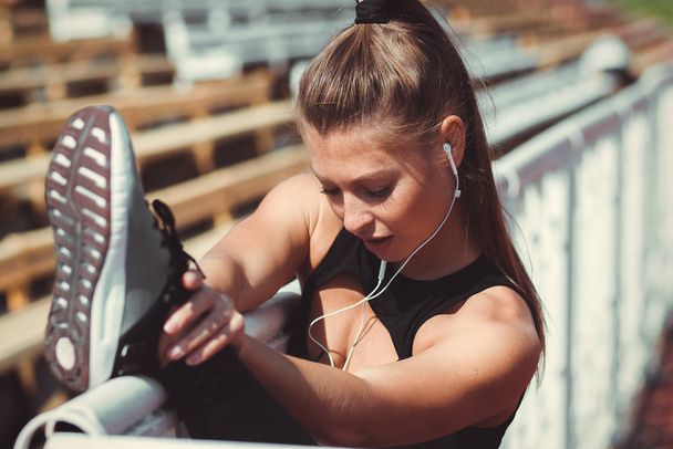 Slim woman with earphones stretching leg on city stadium - Photo, Image
