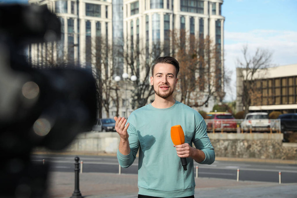 Young male journalist with microphone working on city street - Фото, изображение