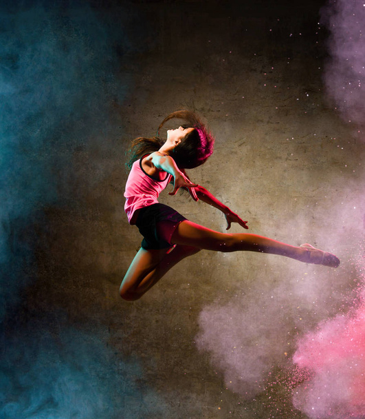 Street dance girl dancer jumping up dancing in neon light doing gymnastic exercises in studio on dark wall - Valokuva, kuva
