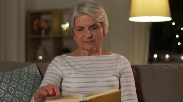 happy senior woman reading book at home in evening - Video