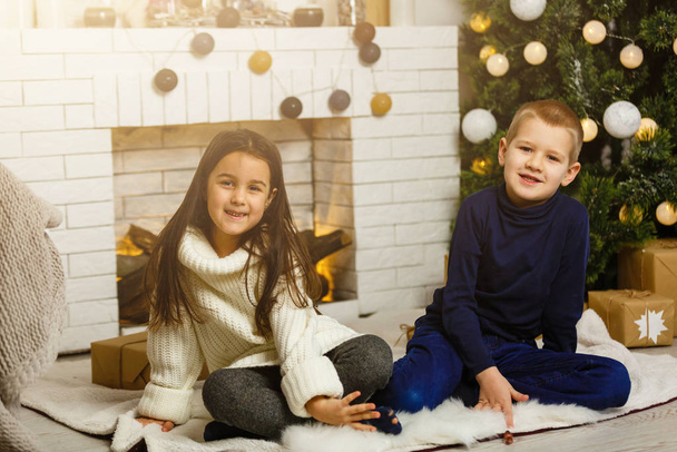 Family on Christmas eve at fireplace. Children under Christmas tree with gift boxes. Decorated living room with traditional fire place. Cozy warm winter evening at home.  - Foto, immagini