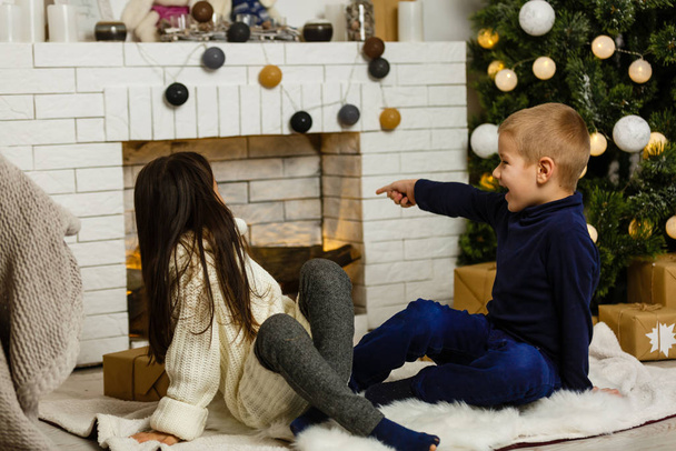 Familie an Heiligabend am Kamin. Kinder unter dem Weihnachtsbaum mit Geschenkschachteln. Dekoriertes Wohnzimmer mit traditionellem Kamin. Gemütlich warmer Winterabend zu Hause.  - Foto, Bild