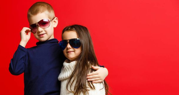 Two happy funny kids standing together and embracing, isolated on red  - Fotoğraf, Görsel